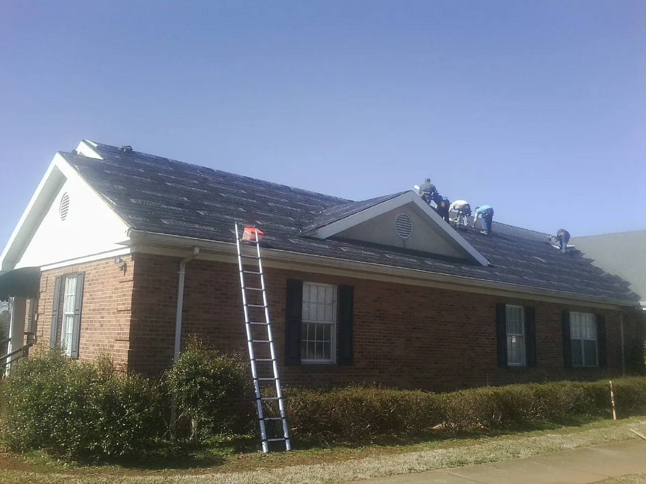 Crew tearing shingles off a brick ranch roof with a ladder set — Metal Roof Repair work by our crew in Anita