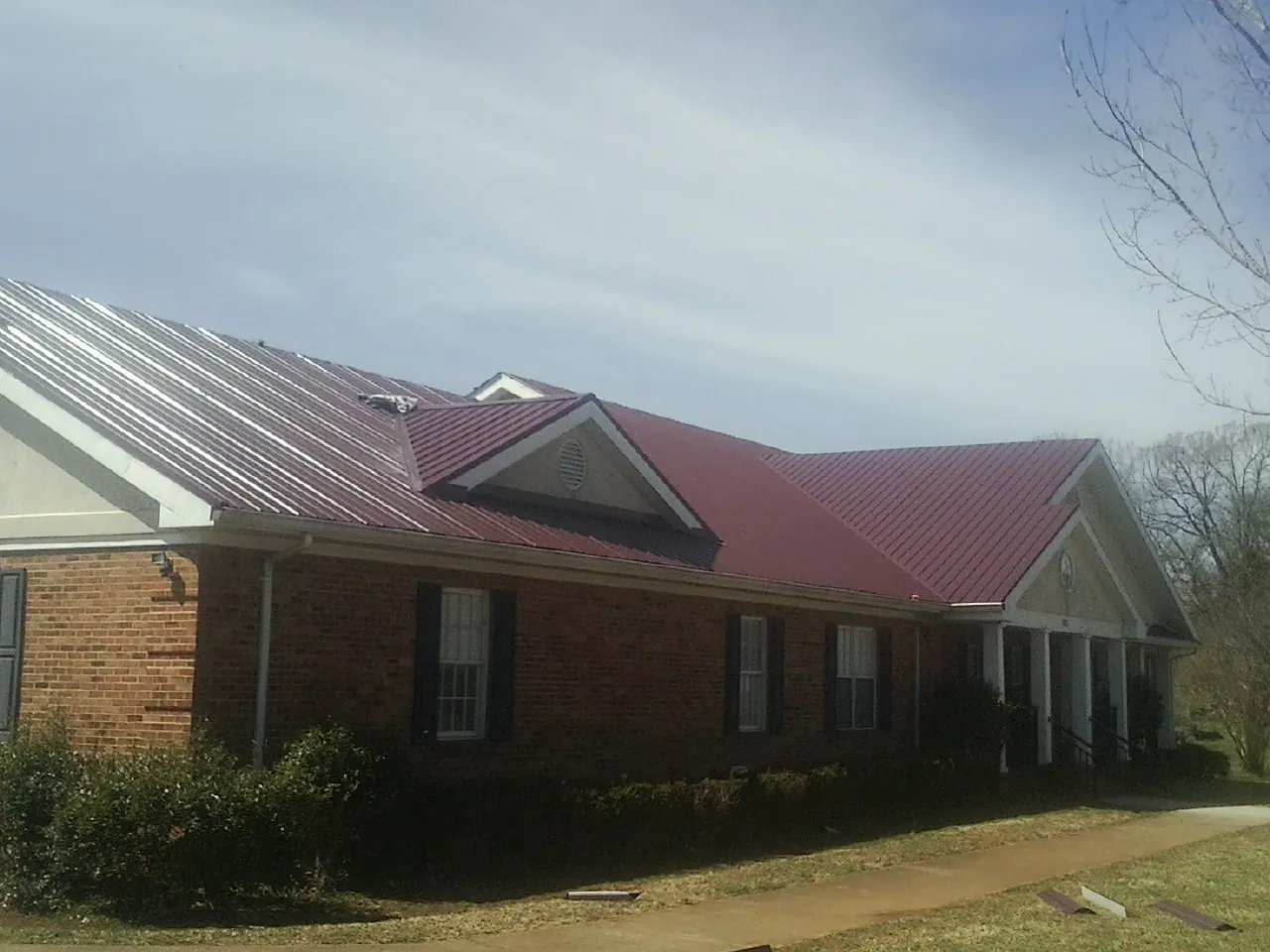 Red metal roof with gabled entries on a long brick building, from a Hail Damage Roof Repair job in Anita