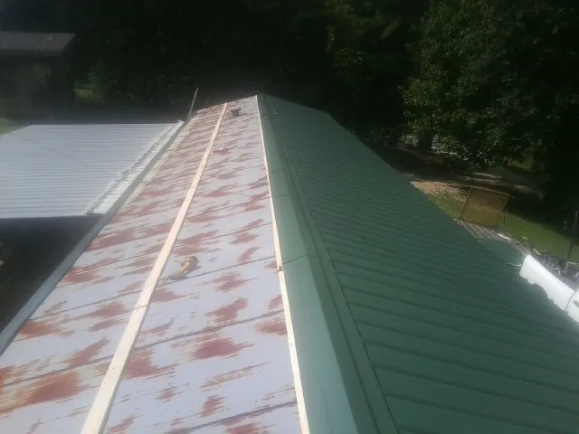 Old rusted panels beside newly installed green metal roofing — Wind Damage Roof Repair by Roofing Brothers in Anita