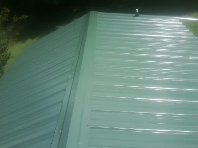 New green metal panels meeting at the ridge of a roof — Flat Roof Repair work by our crew in Anita