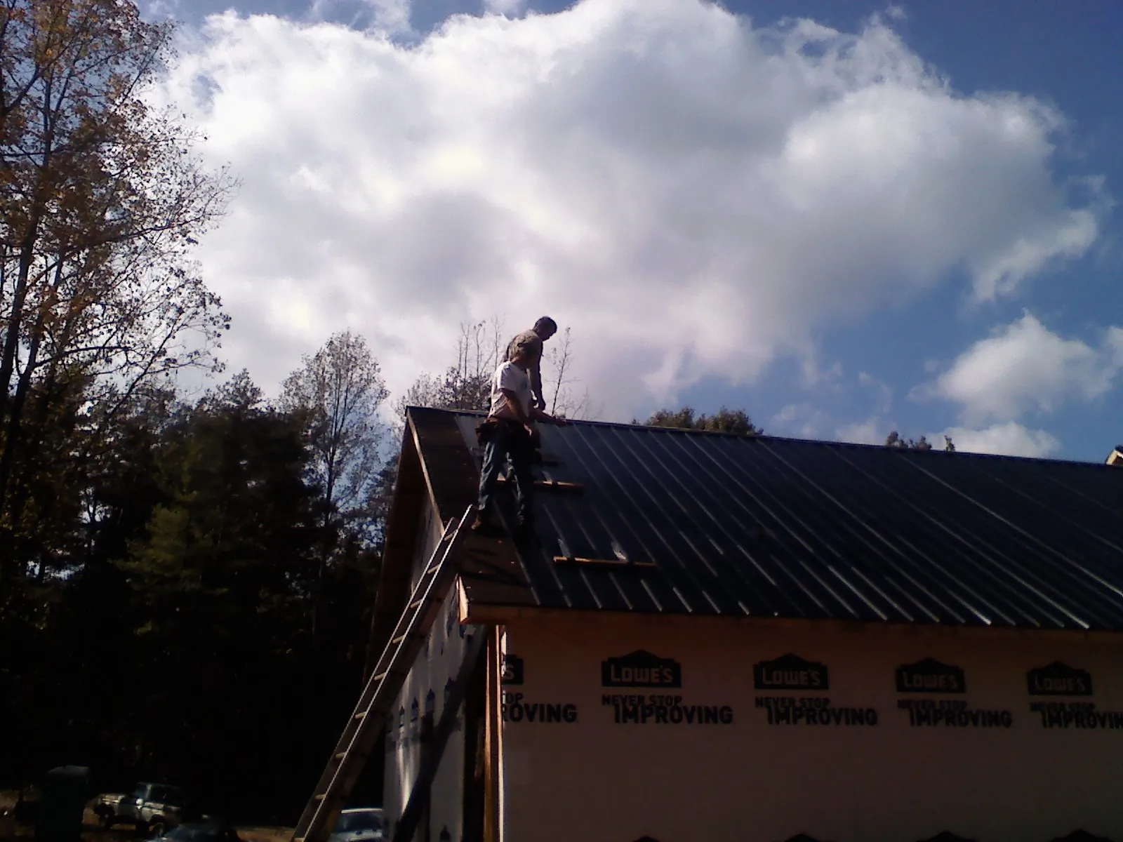 Roofer fastening dark metal panels high against a cloudy sky, from a Roof Inspection job in Anita