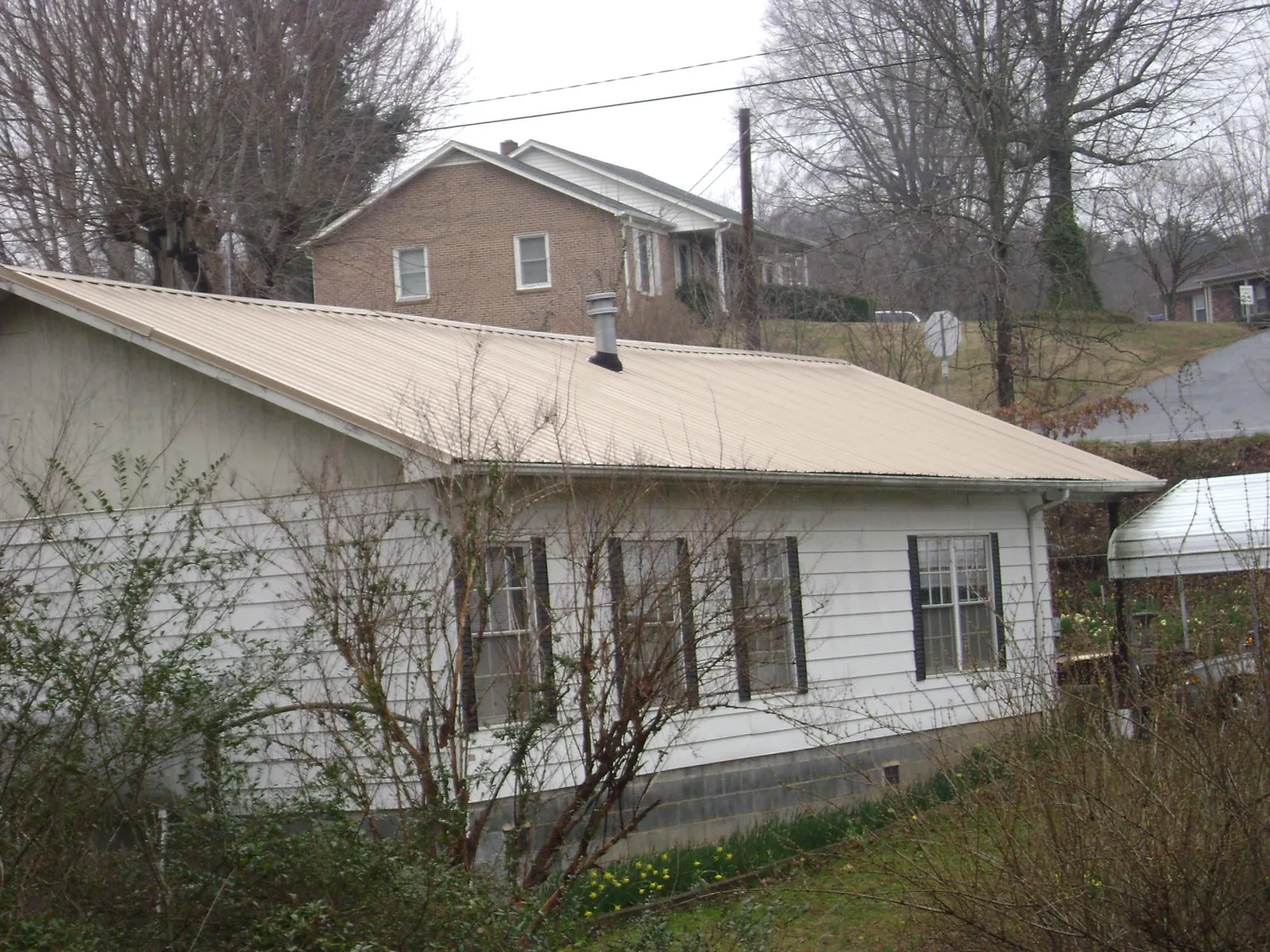 Tan metal roof on a white sided house set into a hillside — Commercial Roofing by Roofing Brothers in Anita